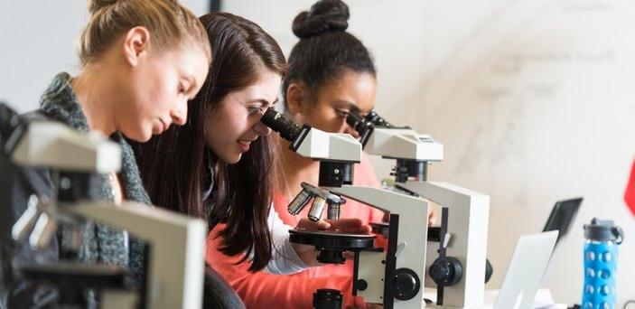 Three students using microscopes in geology lab