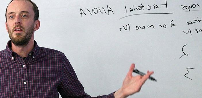A professor speaking to a class in front of a white board
